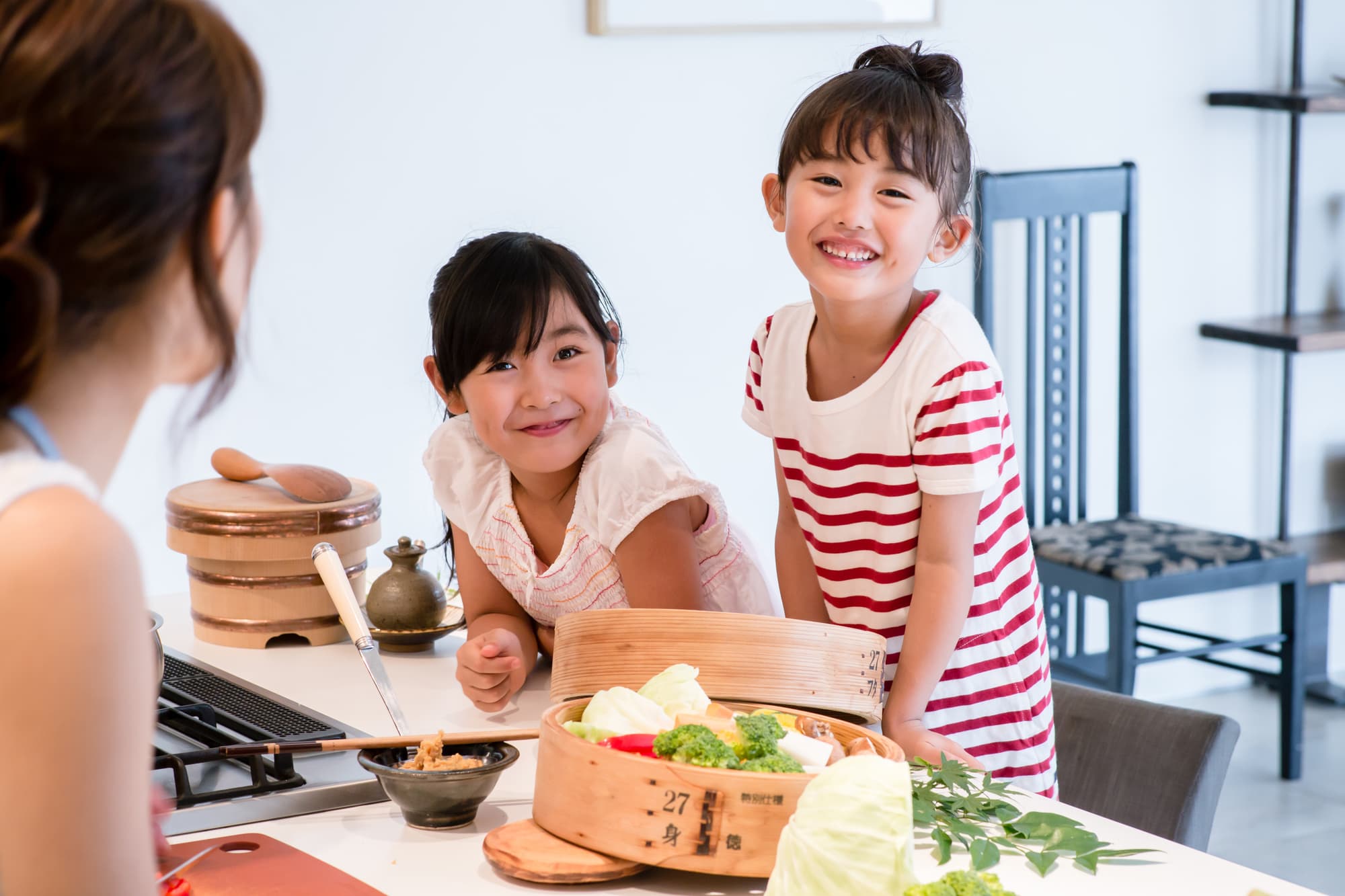 キッチンでお料理する母親と笑顔で会話する姉妹