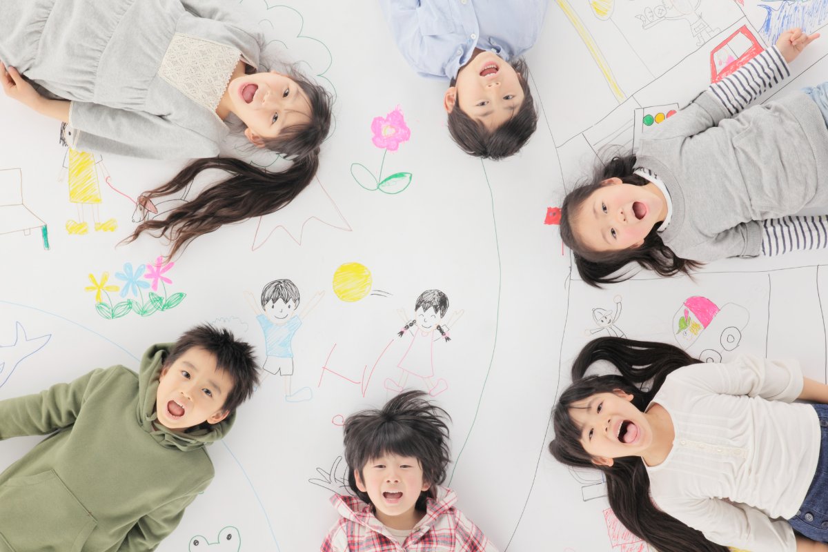 描いた絵の周りに放射状に寝転がる笑顔の子ども達